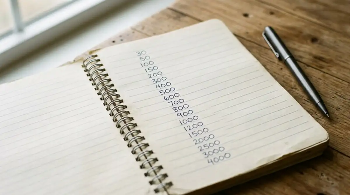 Notizbuch mit handgeschriebenen Zahlenreihen 30, 50, 100, 150 und ein Kugelschreiber daneben