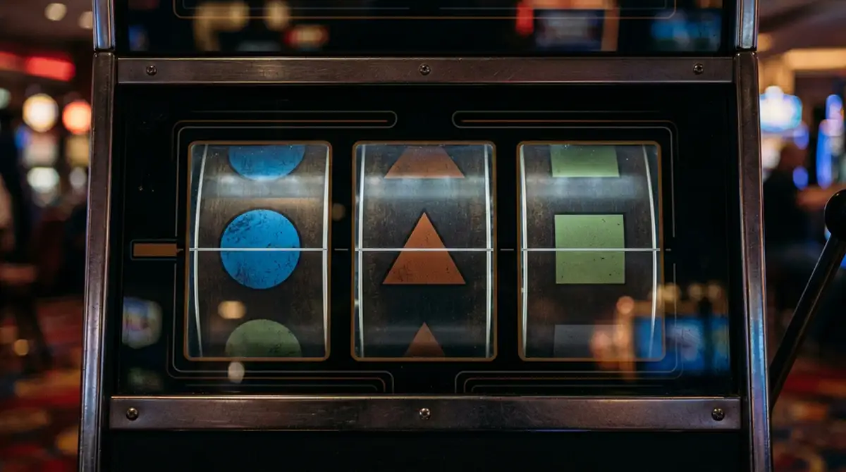 Nahaufnahme eines Spielautomaten-Bildschirms mit drei unspezifischen Walzen voller geometrischer Symbole, leicht verschwommene Hintergrundbeleuchtung, kein Logo, kein konkreter Slot-Name, kein Text